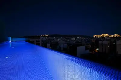 a lit up swimming pool on top of a building at night at Athens Mosaico Suites & Apartments in Athens