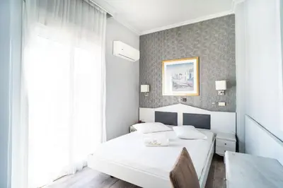 a white bedroom with a bed and a window at Eva Hotel Piraeus in Piraeus