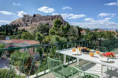 a balcony with a table with fruit and a view of the acropolis at Frixos Acropolis Luxury Apartment in Athens