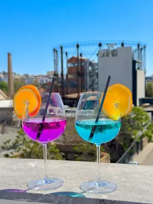 three wine glasses sitting on a table with an orange and blue drink at Ceramus Apartments Gazi View in Athens