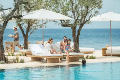 a family sitting on a couch next to a swimming pool at Four Seasons Astir Palace Hotel Athens in Athens