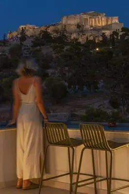 a woman in a white dress standing next to two chairs at Meros - Athenian Residencies in Athens