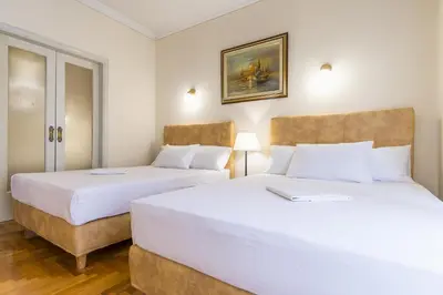 two beds in a room with white walls and wood floors at Victoria Queens Paradise Apartments in Athens