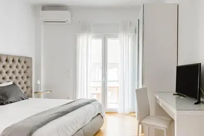 a white bedroom with a bed and a desk and a television at Bright and roomy apartment, in the heart of Athens in Athens