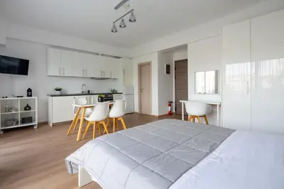 a white bedroom with a large bed and a kitchen at Boutique Studios near Airport in Pallíni