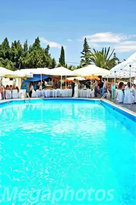 a large blue swimming pool with white chairs and umbrellas at Anna Studios in Agia Marina Aegina