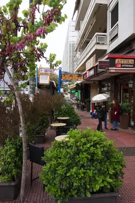 a woman walking down a city street with an umbrella at Museum of Modern Art Rooms in apartment, next to metro Suggrou Fix, walk to Acropolis in Athens