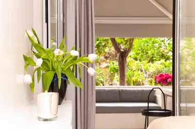 a vase of flowers on a table next to a window at Sweet Suite Flora in Vouliagmeni in Athens