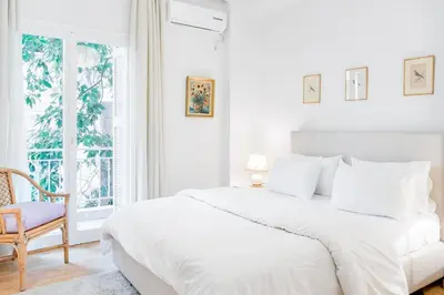 a white bedroom with a bed and a chair at Koukaki Apartment with a Sunny Balcony, near the Acropolis in Athens
