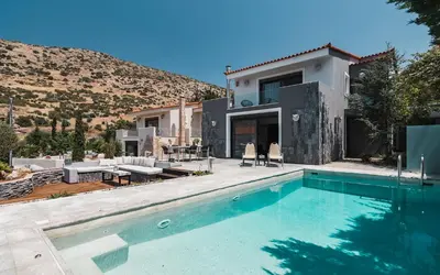 a villa with a swimming pool in front of a house at Adam & Eve Villas in Sounio