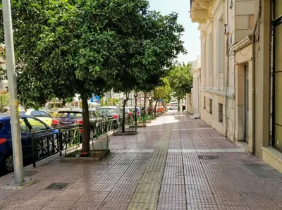 a street with parked cars and a tree on a sidewalk at A Refreshed & Rich in Details Apartment in Piraeus (Passalimani - Marina Zeas) in Piraeus
