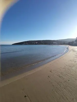 a beach with a group of people walking in the water at Finikas Rooms in Agia Marina Aegina