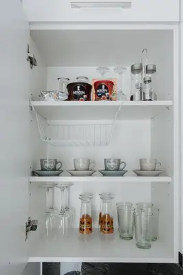 a white pantry with glass vases and bowls on shelves at Nest Apartment in Athens
