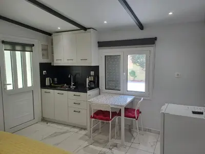 a kitchen with white cabinets and a table and a window at Vicky's place,near Athens airport in Koropíon