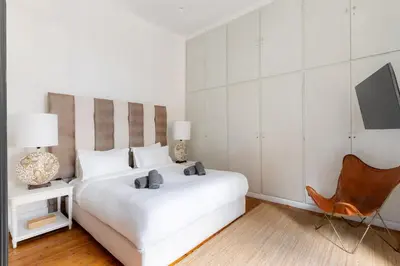 a white bedroom with a white bed and a chair at Art Pantheon - Suites & Apartments in Athens