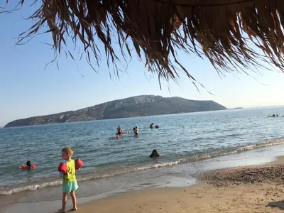 a young boy standing on the beach with people in the water at Seaview 2nd flr. apt. next to the beach, wifi,a/c,p/c media. in Anavissos