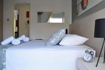 a bed with white pillows and a clock on it at Poseidon by Heloni Apartments in Piraeus