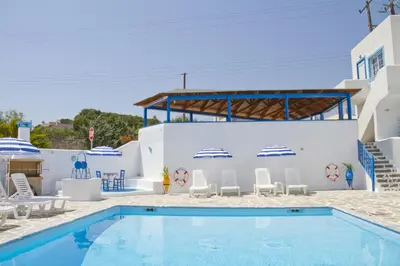 a swimming pool with chairs and a building at Blue Dolphin Studios and Apartment in Vaia