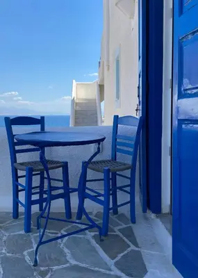 a blue table and chairs with the ocean in the background at Blue Dolphin Studios and Apartment in Vaia