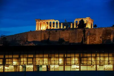 a building lit up at night with a building in the background at Acropolis amazing balcony view 3 minutes walking to the museum in Athens