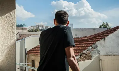 a man standing on a balcony looking out at the city at 2 BEDROOM APARTMENT AT THE HISTORICAL CENTER, VIEW TO ACROPOLIS in Athens