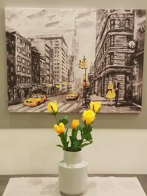a vase with yellow flowers in front of a painting at Golden Aurora - Modern Apartment in Egaleo-Athens in Athens