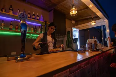 a woman standing at a bar making a drink at Athens Hawks in Athens