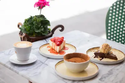 a table with three plates of desserts and cups of coffee at St. Bjur Suites in Athens