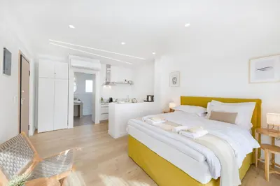 a white bedroom with a large bed and a kitchen at Maryflower Premium Apartments Piraeus in Piraeus