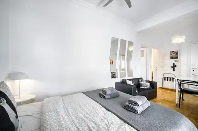 a white bedroom with a bed and a black chair at The Cactus Apartment with Large Sunny Balcony in Athens