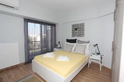 a white bedroom with a large bed and a window at Edem Beach Apartment with Mountain View by Athenian Homes in Athens