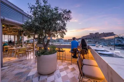 a rooftop patio with a tree and people sitting at tables at Niche Hotel Athens in Athens