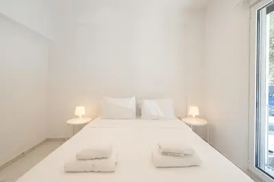 a white bedroom with a white bed with two lamps at Sophisticated Modern Apt in Athens center in Athens