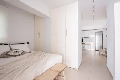 a white bedroom with a bed and a wooden bench at Bliss Living in Vouliagmeni