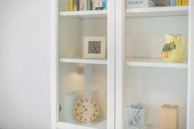 a white book shelf with a clock and books at Fresh and Clean apt for 6 in Koukaki in Athens