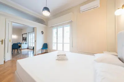 a white bedroom with a bed and a living room at Athens Empire Paradise Apartment in Athens