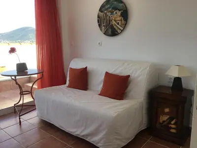 a living room with a white couch with two orange pillows at Bay watch Apartment close to the airport at PORTO RAFTI in Porto Rafti
