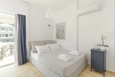 a white bedroom with a bed and a window at Bay watch Apartment close to the airport at PORTO RAFTI in Porto Rafti