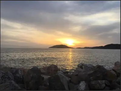 a sunset over a large body of water with rocks at Sea Side Apartment in Palaiá Fókaia