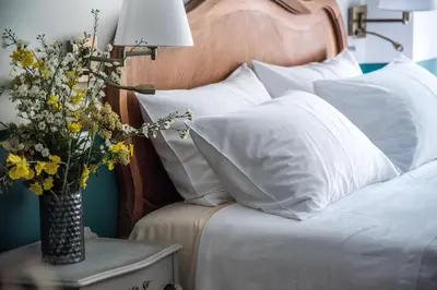 a bed with white pillows and a vase of flowers on a table at Rastoni Athens Suites near Acropolis at Tsatsou street in Athens