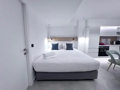 a white bedroom with a white bed and a chair at PINACOTA SUITES ATHENS in Athens