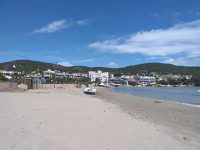a beach with a boat sitting on the sand at agia marina riviera aigina in Agia Marina Aegina