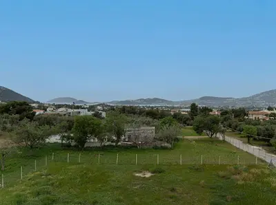 a field with a fence and trees and a town at Yellow house in Palaiá Fókaia