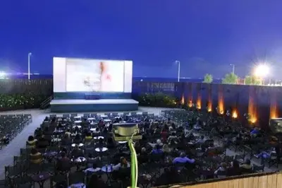 a crowd of people sitting in front of a large screen at SEASIDE SUNSET WALKS in Athens