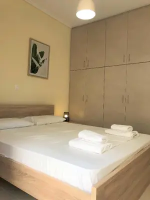 a bedroom with a bed with white sheets and cabinets at Boho Apartment near Athens Airport in Spáta