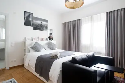 a white bedroom with a large bed and a chair at Syntagma Rita apartment 2 in Athens