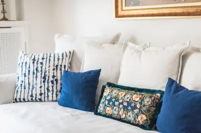 a white couch with blue pillows on it at NEW! Bright & Remodeled 1Bed apt 2min Walk to Acropolis in Athens