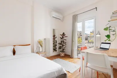 a white bedroom with a bed and a desk with a laptop at Studio with sunny balcony in Exarcheia in Athens