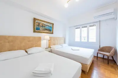 two beds in a white room with a chair at Victoria Queens Suites Apartments in Athens