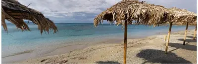 a straw umbrella on a beach with the water at Scorpios Sea Side Hotel in Piraeus